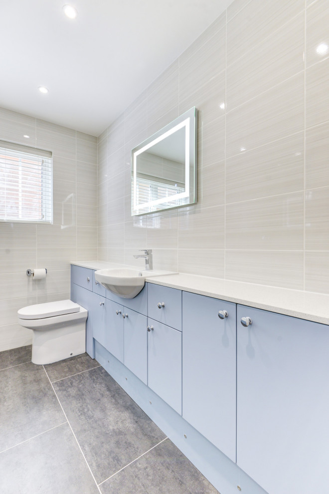Bathroom - mid-sized contemporary kids' beige tile and ceramic tile gray floor and single-sink bathroom idea in Sussex with flat-panel cabinets, blue cabinets, a wall-mount toilet, beige walls, an integrated sink, laminate countertops, white countertops and a built-in vanity