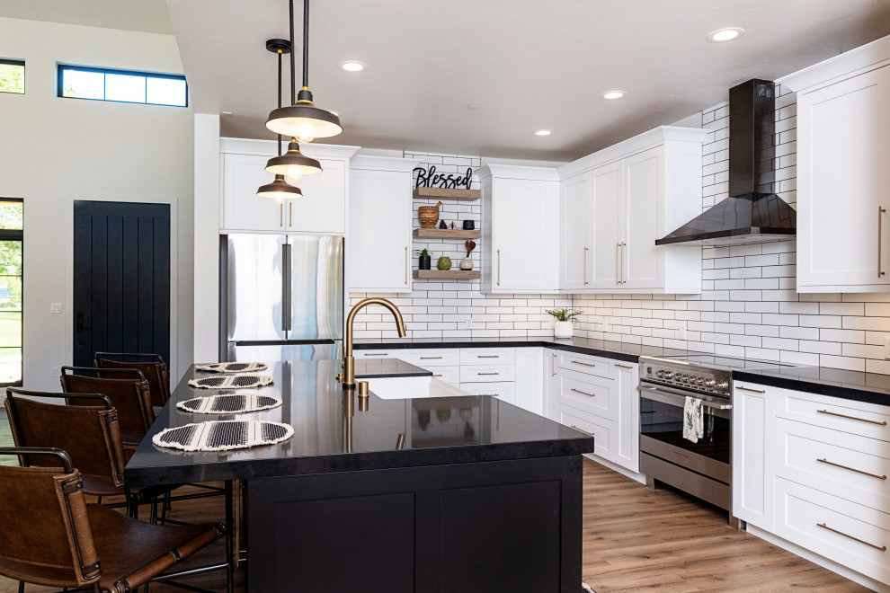 This is an example of a large country l-shaped open plan kitchen in Sacramento with an undermount sink, shaker cabinets, black cabinets, quartz benchtops, white splashback, subway tile splashback, stainless steel appliances, light hardwood floors, with island, brown floor, black benchtop and vaulted.