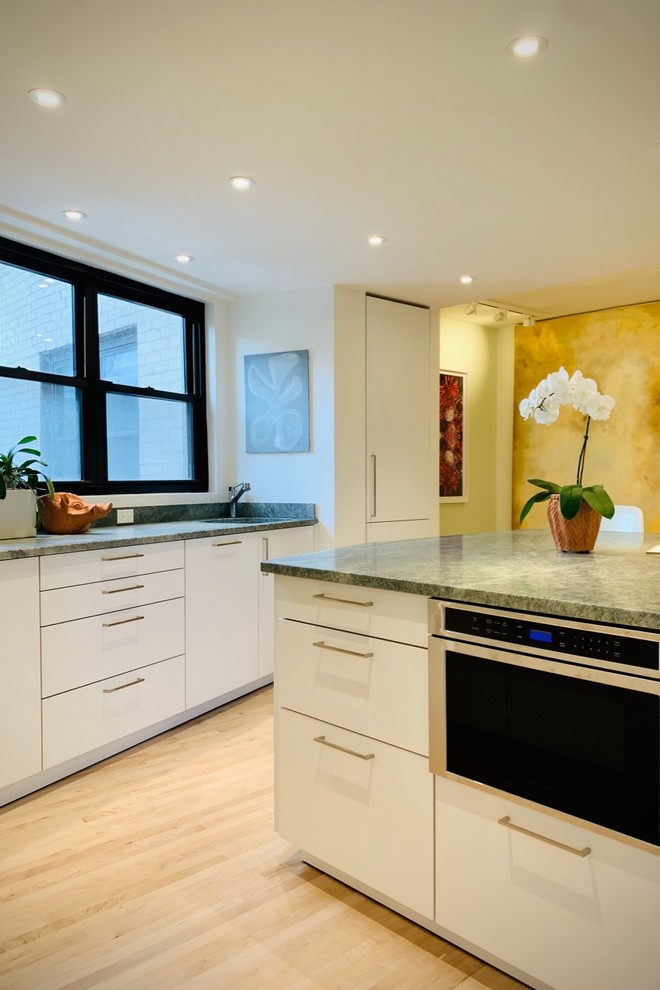 Mid-sized modern l-shaped open plan kitchen in New York with an undermount sink, flat-panel cabinets, white cabinets, soapstone benchtops, multi-coloured splashback, stone slab splashback, stainless steel appliances, light hardwood floors, with island, beige floor and multi-coloured benchtop.