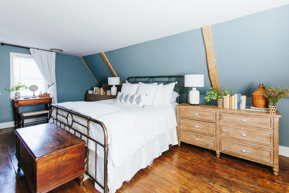 Exemple d'une grande chambre parentale chic avec un mur bleu, un sol en bois brun, une cheminée standard, un manteau de cheminée en plâtre, un sol marron et poutres apparentes.