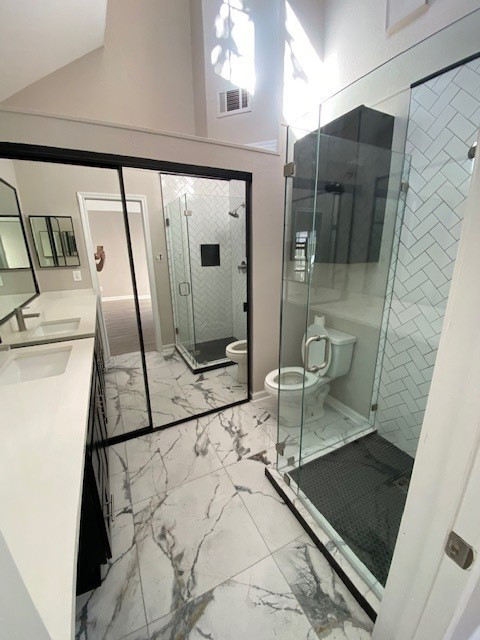 Bathroom remodel, herringbone shower subway tiles with black hexagon small tile on shower flooring.  Frameless shower doors. Black cabinets. Porcelain 24x24 tile flooring