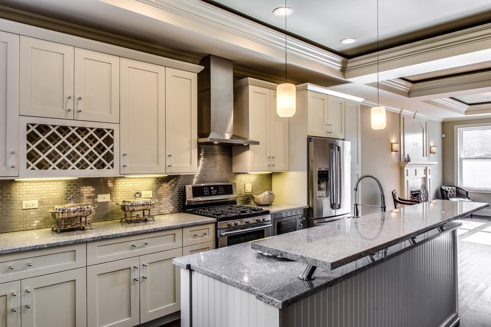 This is an example of a traditional galley open plan kitchen in Chicago with stainless steel appliances, shaker cabinets, white cabinets, metallic splashback and mosaic tile splashback.