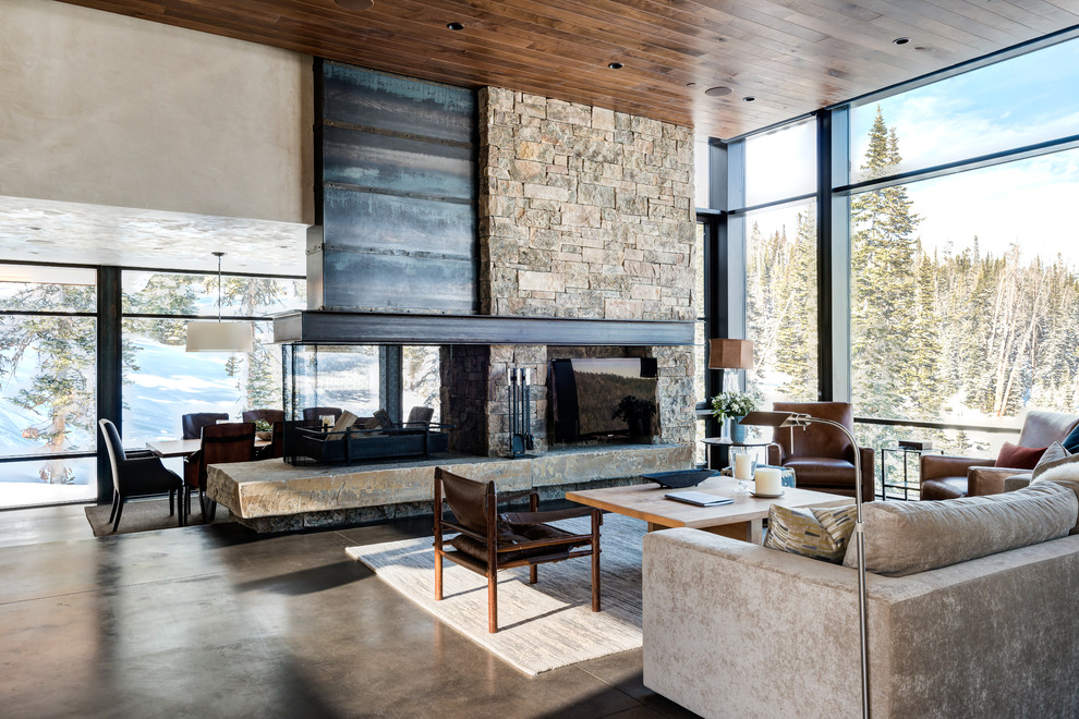 Expansive contemporary open concept living room in Other with beige walls, concrete floors, a two-sided fireplace, a stone fireplace surround and a freestanding tv.