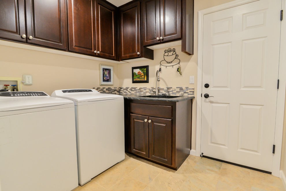 This is an example of a mid-sized traditional l-shaped dedicated laundry room in Portland with an undermount sink, raised-panel cabinets, dark wood cabinets, granite benchtops, beige walls, porcelain floors and a side-by-side washer and dryer.