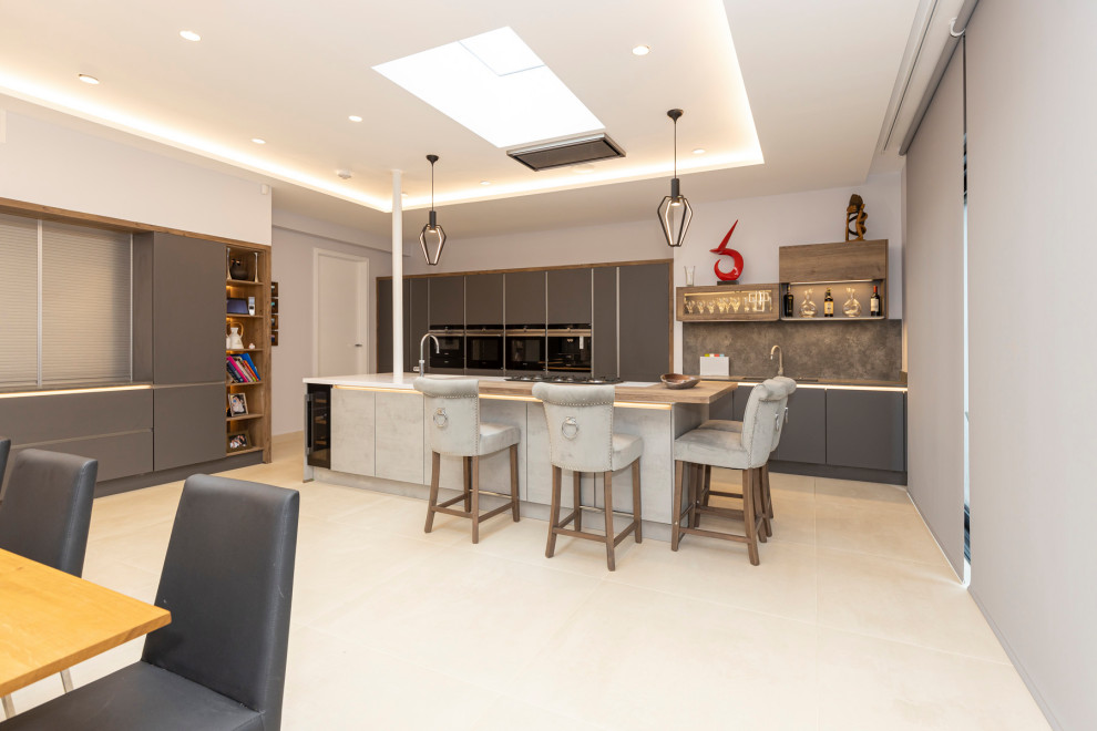 Large minimalist l-shaped porcelain tile, white floor and tray ceiling eat-in kitchen photo in Hertfordshire with a single-bowl sink, flat-panel cabinets, gray cabinets, quartzite countertops, gray backsplash, cement tile backsplash, black appliances, an island and gray countertops