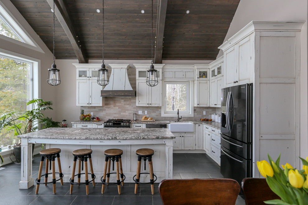 Large country l-shaped eat-in kitchen in Toronto with a farmhouse sink, shaker cabinets, distressed cabinets, granite benchtops, beige splashback, brick splashback, stainless steel appliances, ceramic floors, with island, grey floor, multi-coloured benchtop and exposed beam.