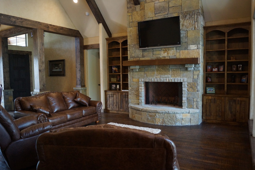 This is an example of a mid-sized country open concept living room in Dallas with beige walls, dark hardwood floors, a standard fireplace, a stone fireplace surround and a wall-mounted tv.