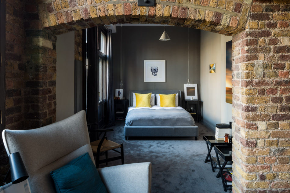 ロンドンにある広いインダストリアルスタイルのおしゃれな主寝室 (マルチカラーの壁、カーペット敷き、グレーの床、レンガ壁) のインテリア