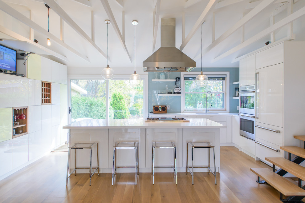 Photo of a large contemporary l-shaped kitchen in Toronto with an undermount sink, flat-panel cabinets, white cabinets, blue splashback, glass sheet splashback, panelled appliances, light hardwood floors and with island.