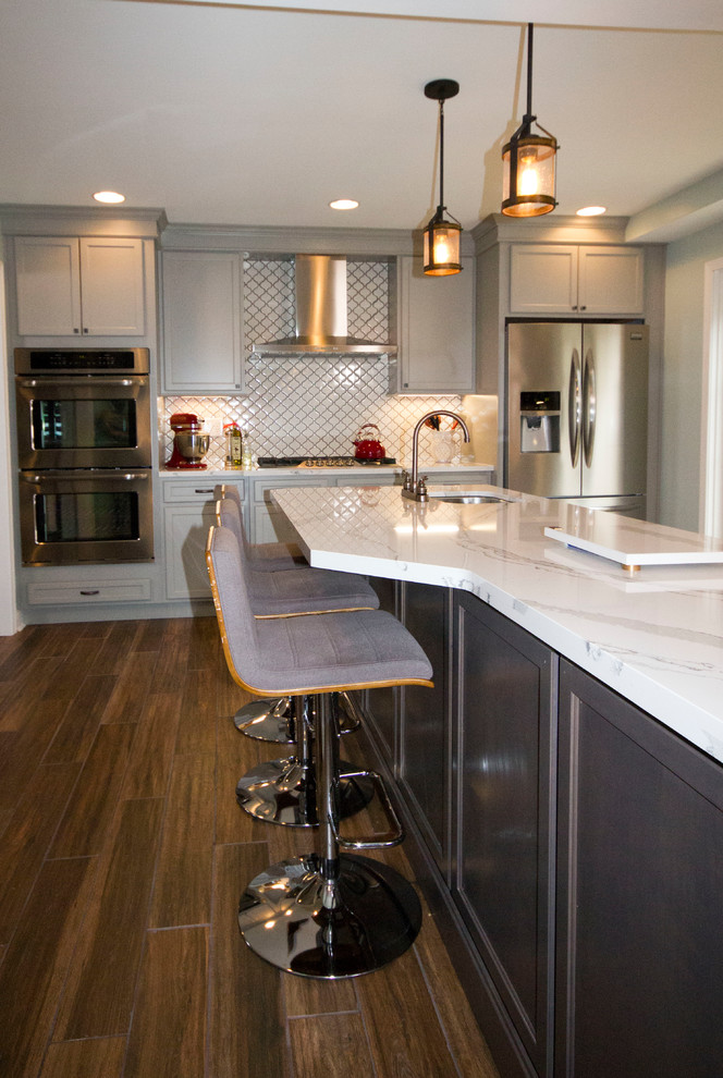 Enclosed kitchen - large transitional l-shaped medium tone wood floor and brown floor enclosed kitchen idea in Cincinnati with a farmhouse sink, recessed-panel cabinets, gray cabinets, marble countertops, white backsplash, porcelain backsplash, stainless steel appliances and an island