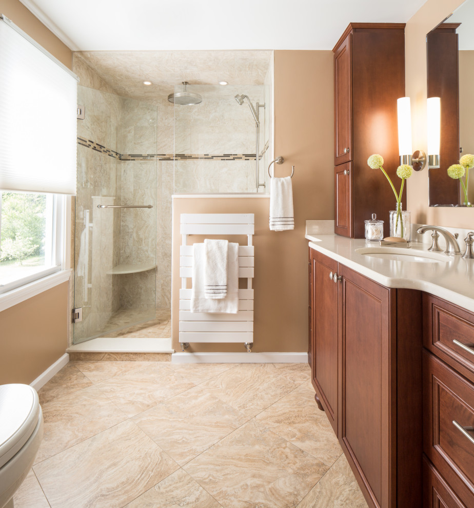 This is an example of a mid-sized traditional master bathroom in Boston with recessed-panel cabinets, medium wood cabinets, an alcove shower, a one-piece toilet, beige tile, travertine, beige walls, travertine floors, an undermount sink, solid surface benchtops, beige floor, a hinged shower door and white benchtops.