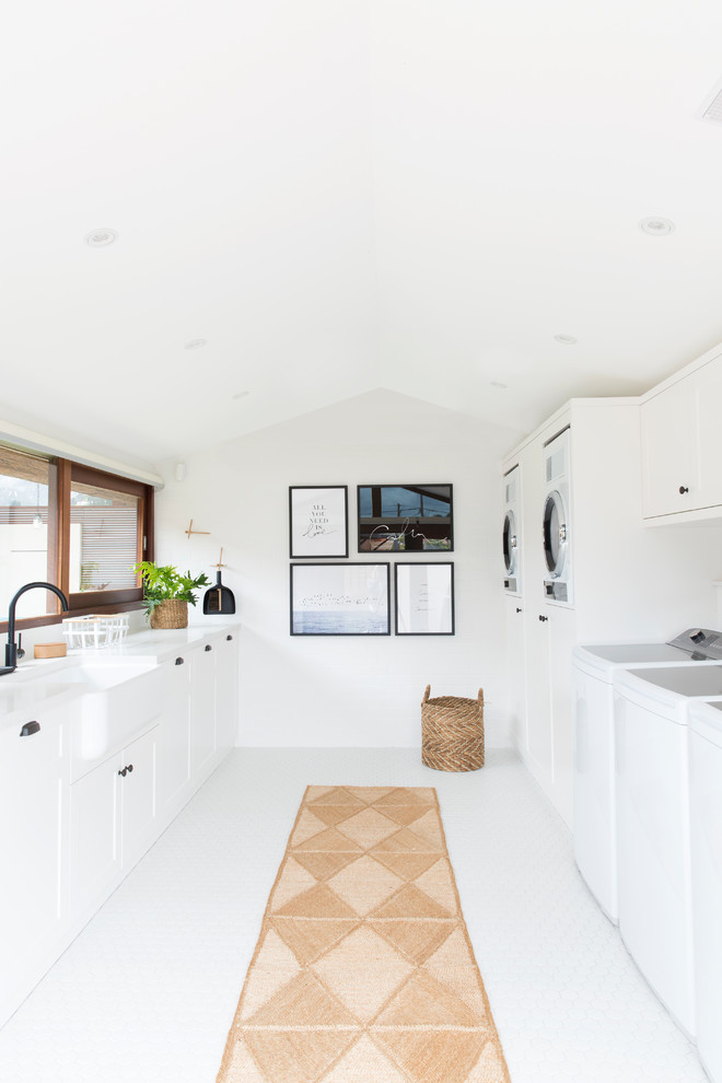 Photo of an expansive contemporary galley dedicated laundry room in Gold Coast - Tweed with a farmhouse sink, shaker cabinets, white cabinets, quartz benchtops, white walls, porcelain floors, white floor and a side-by-side washer and dryer.