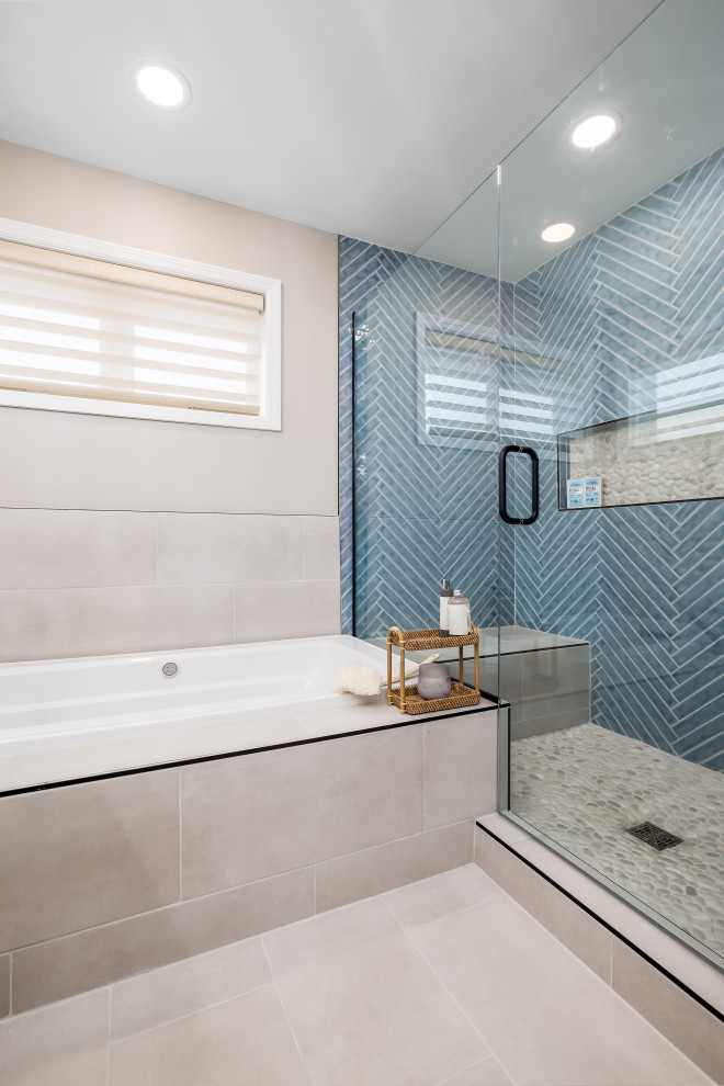 Photo of a large coastal ensuite bathroom in Minneapolis with flat-panel cabinets, light wood cabinets, a built-in bath, an alcove shower, a one-piece toilet, blue tiles, ceramic tiles, beige walls, porcelain flooring, a submerged sink, marble worktops, beige floors, a hinged door, white worktops, a laundry area, double sinks, a freestanding vanity unit and wallpapered walls.