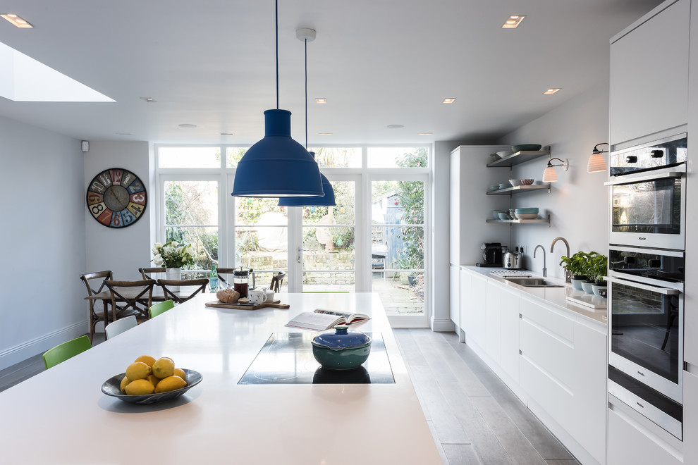 Inspiration for a large modern single-wall open plan kitchen in London with flat-panel cabinets, white cabinets, stainless steel appliances, light hardwood floors and with island.