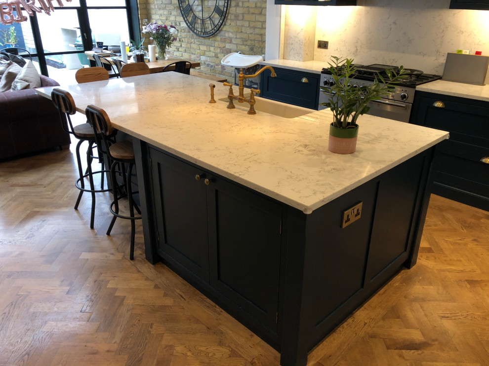 This is an example of a mid-sized country single-wall eat-in kitchen in Surrey with beaded inset cabinets, blue cabinets, quartzite benchtops, stainless steel appliances, medium hardwood floors, with island and white benchtop.