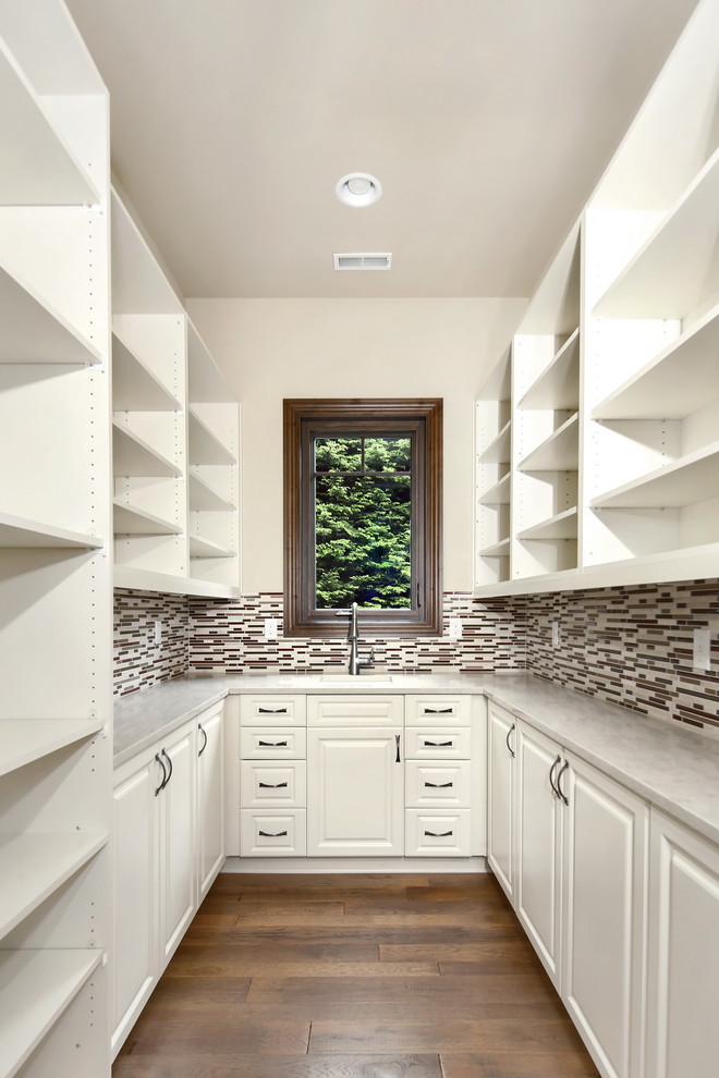 Design ideas for a mid-sized mediterranean u-shaped kitchen pantry in Seattle with an undermount sink, raised-panel cabinets, white cabinets, quartz benchtops, multi-coloured splashback, matchstick tile splashback, medium hardwood floors, no island, brown floor and white benchtop.