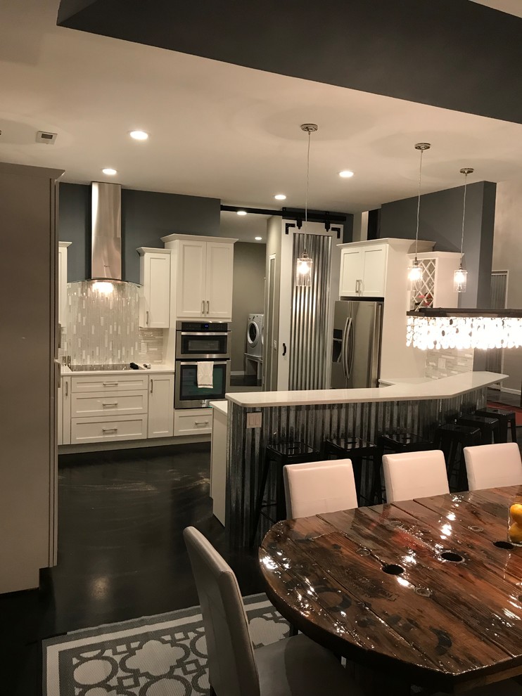 Contemporary eat-in kitchen in Other with a farmhouse sink, shaker cabinets, white cabinets, quartzite benchtops, white splashback, glass tile splashback, stainless steel appliances, concrete floors, a peninsula and black floor.