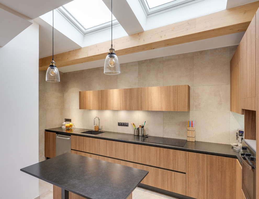 Mid-sized contemporary l-shaped kitchen in Marseille with a single-bowl sink, light wood cabinets, with island, beige floor, black benchtop, flat-panel cabinets, beige splashback and stainless steel appliances.