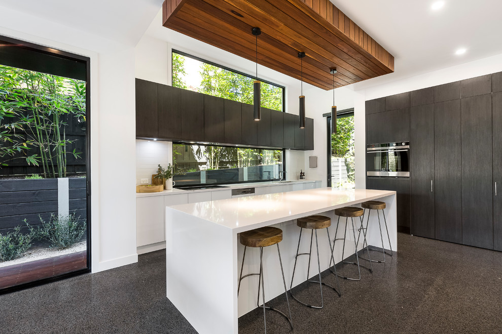 This is an example of a contemporary l-shaped open plan kitchen in Melbourne with flat-panel cabinets, white splashback, glass sheet splashback, black appliances, terrazzo floors, with island and grey floor.