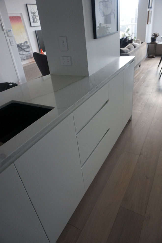 Inspiration for a medium sized modern galley open plan kitchen in Sydney with a submerged sink, flat-panel cabinets, white cabinets, engineered stone countertops, white splashback, engineered quartz splashback, stainless steel appliances, medium hardwood flooring, an island and white worktops.