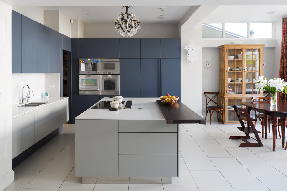 Mid-sized contemporary l-shaped eat-in kitchen in London with an undermount sink, flat-panel cabinets, blue cabinets, white splashback, panelled appliances, with island and white floor.