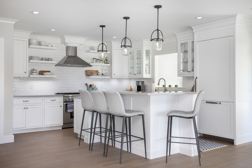 This is an example of a transitional l-shaped kitchen in Boston with shaker cabinets, white cabinets, white splashback, panelled appliances, medium hardwood floors, with island, brown floor and grey benchtop.