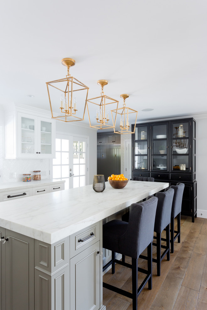 Large transitional l-shaped light wood floor open concept kitchen photo in Orange County with a farmhouse sink, shaker cabinets, white cabinets, marble countertops, white backsplash, brick backsplash, stainless steel appliances and an island