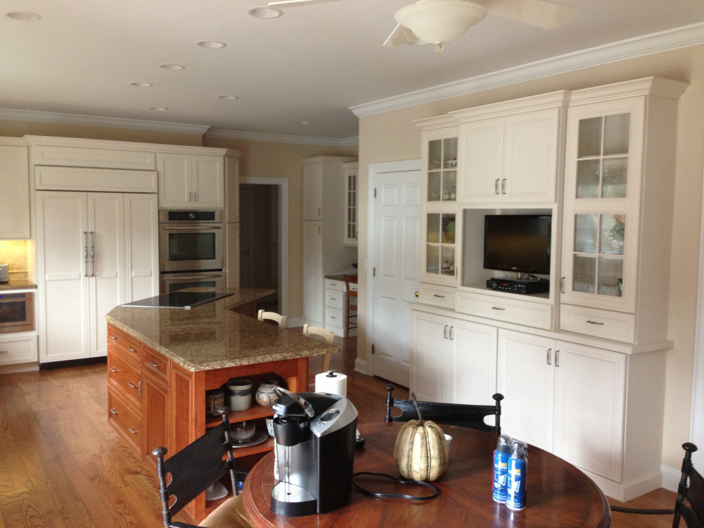 Example of a large transitional u-shaped medium tone wood floor and brown floor eat-in kitchen design in New York with an undermount sink, shaker cabinets, white cabinets, granite countertops, white backsplash, porcelain backsplash, stainless steel appliances, an island and multicolored countertops