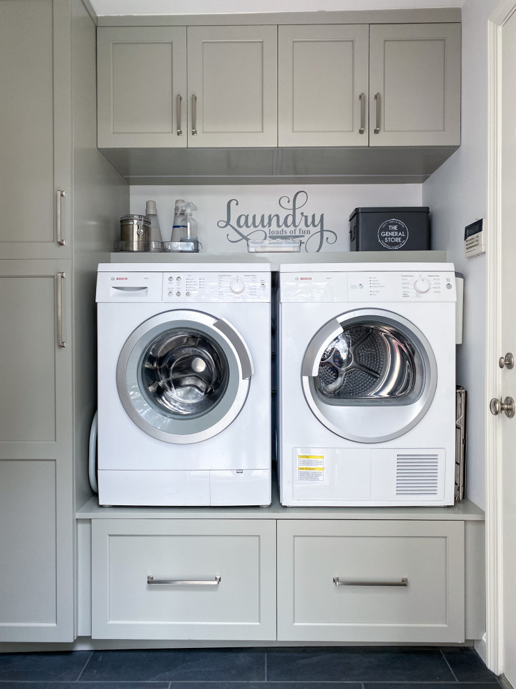Diseño de lavadero lineal clásico renovado con puertas de armario grises, paredes grises, suelo de baldosas de porcelana, lavadora y secadora juntas y suelo negro