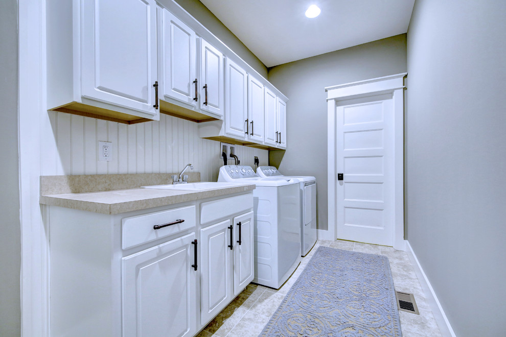 Photo of a mid-sized transitional single-wall dedicated laundry room in Other with a drop-in sink, raised-panel cabinets, white cabinets, laminate benchtops, grey walls, ceramic floors, a side-by-side washer and dryer, beige floor and beige benchtop.