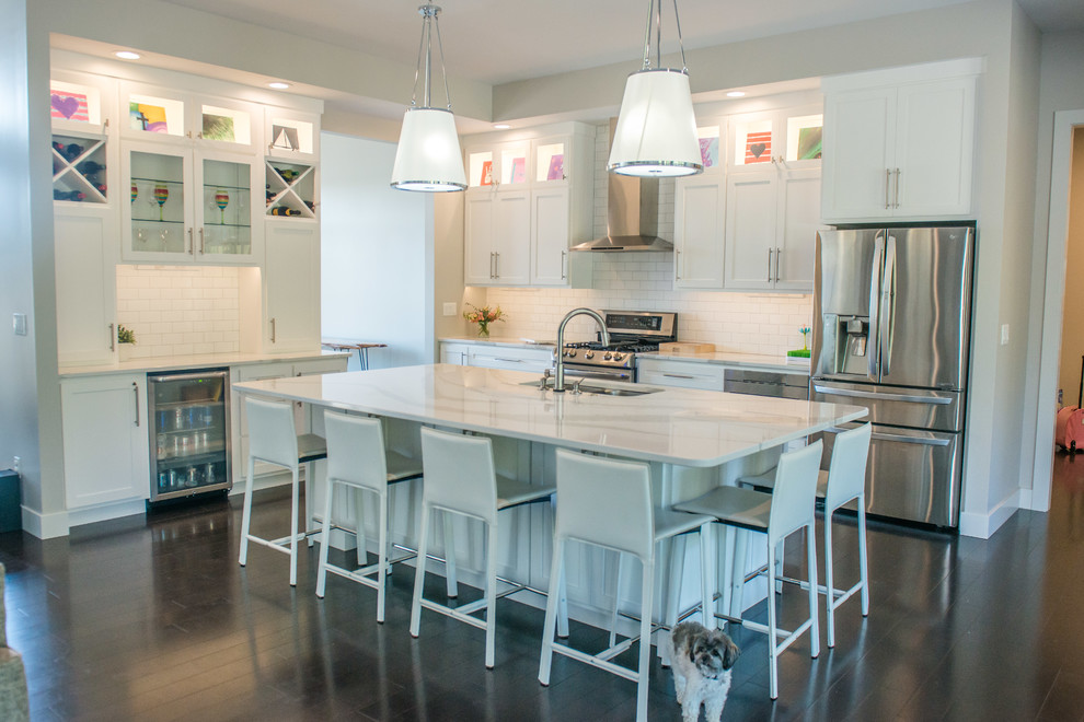 Example of a huge transitional l-shaped dark wood floor and brown floor open concept kitchen design with a double-bowl sink, shaker cabinets, white cabinets, quartz countertops, white backsplash, ceramic backsplash, stainless steel appliances and an island