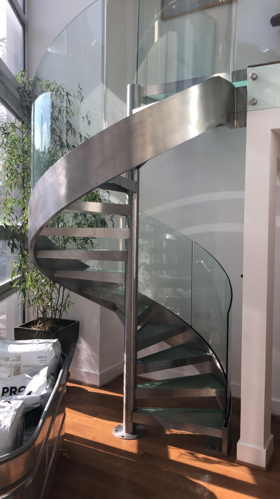 Photo of a mid-sized contemporary glass spiral staircase in DC Metro with open risers, glass railing and wood walls.