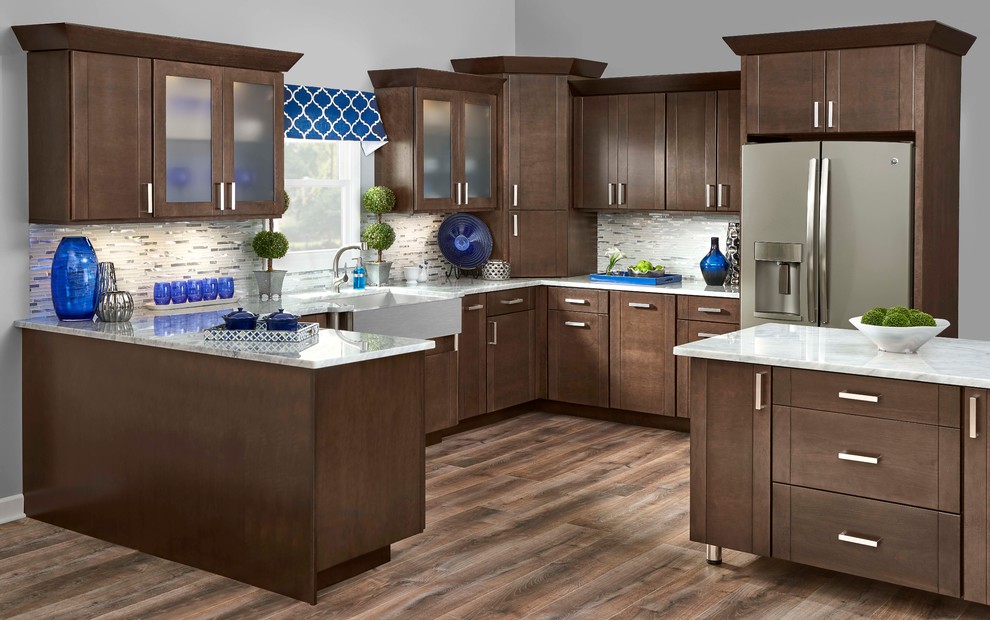 Mid-sized transitional u-shaped medium tone wood floor and brown floor enclosed kitchen photo in Orange County with a farmhouse sink, shaker cabinets, medium tone wood cabinets, marble countertops, white backsplash, matchstick tile backsplash, stainless steel appliances and a peninsula