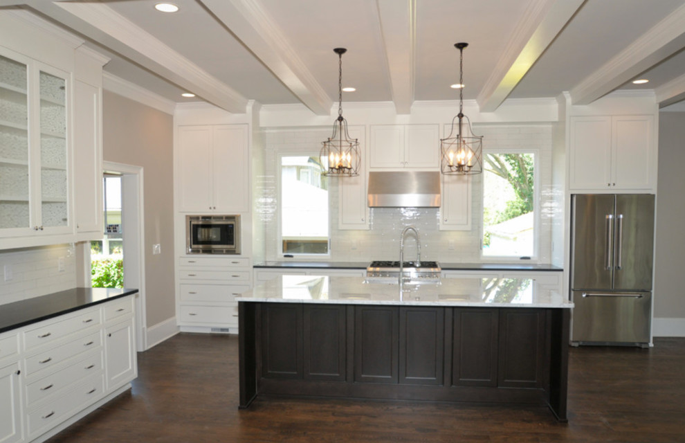 Open concept kitchen - large transitional l-shaped dark wood floor and brown floor open concept kitchen idea in Atlanta with shaker cabinets, white cabinets, an island, a farmhouse sink, quartzite countertops, white backsplash, ceramic backsplash and stainless steel appliances