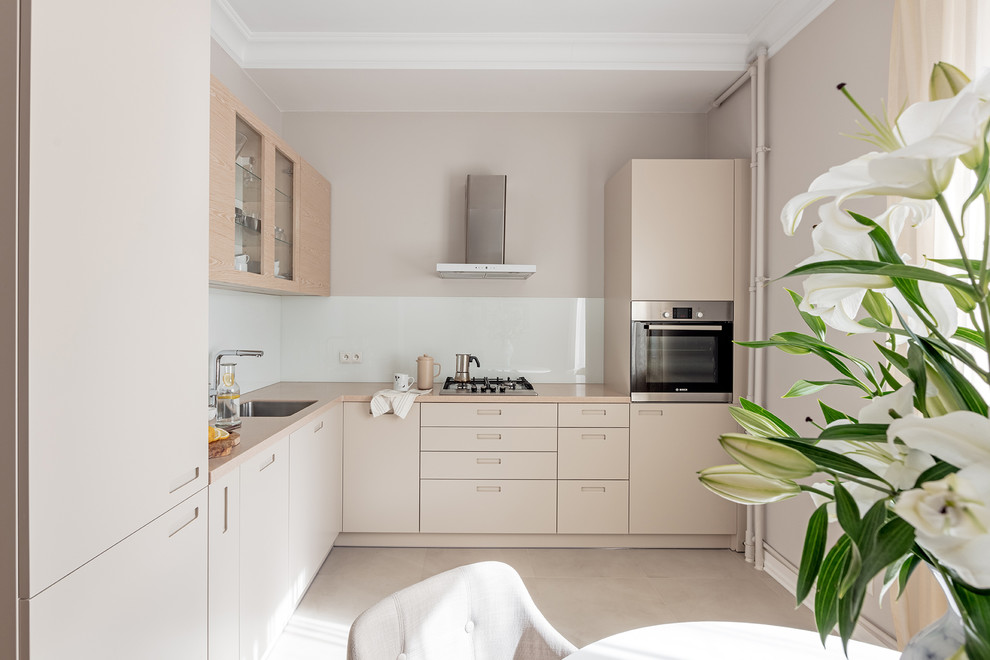 This is an example of a small modern l-shaped eat-in kitchen in Other with an undermount sink, flat-panel cabinets, beige cabinets, quartz benchtops, white splashback, glass sheet splashback, stainless steel appliances, ceramic floors and no island.