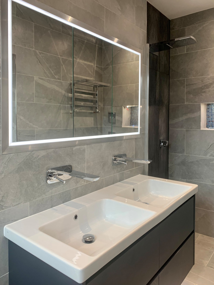 Design ideas for a mid-sized master wet room bathroom in Hertfordshire with flat-panel cabinets, blue cabinets, a wall-mount toilet, gray tile, porcelain tile, grey walls, porcelain floors, a wall-mount sink, grey floor, an open shower, a niche, a double vanity, a floating vanity and coffered.
