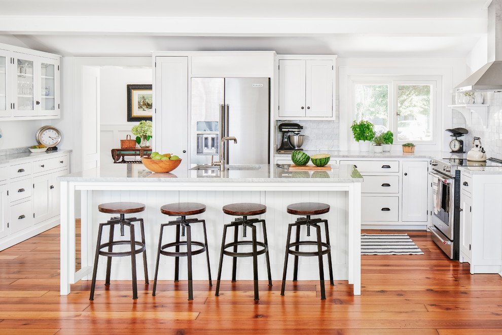 This is an example of a mid-sized beach style u-shaped open plan kitchen in Toronto with an undermount sink, shaker cabinets, white cabinets, marble benchtops, grey splashback, stone tile splashback, stainless steel appliances, medium hardwood floors, with island, brown floor and grey benchtop.