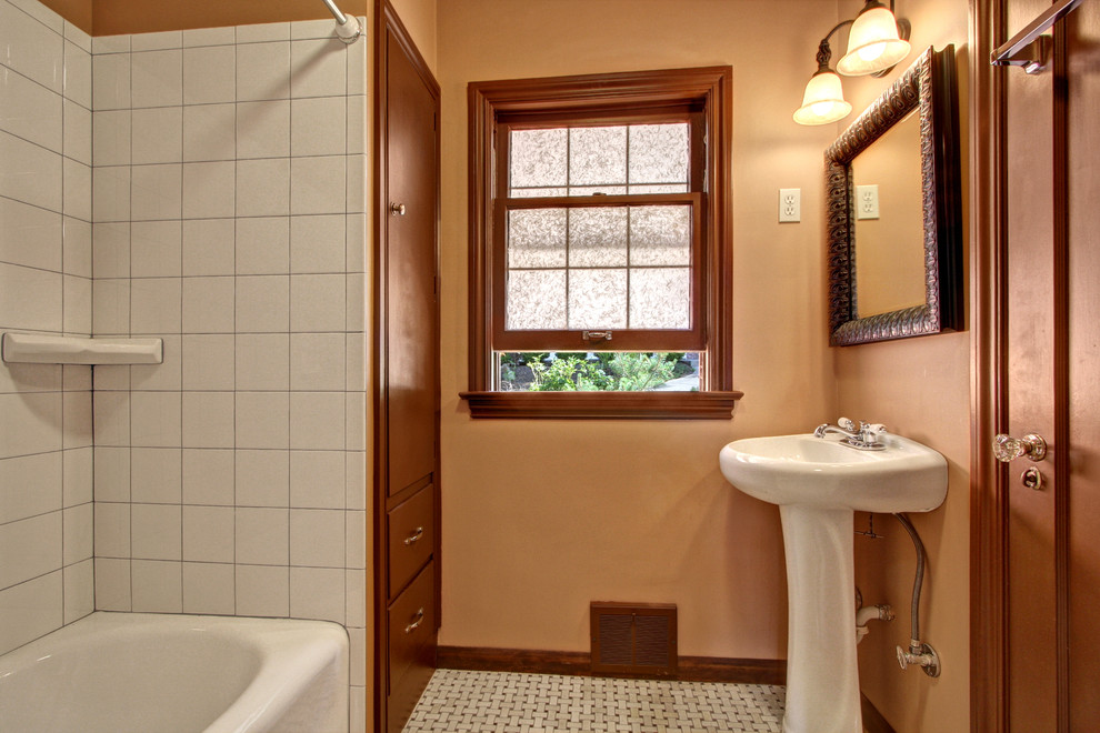 Mid-sized traditional bathroom in Seattle with a pedestal sink, flat-panel cabinets, brown cabinets, a drop-in tub, a shower/bathtub combo, a one-piece toilet, beige tile, stone tile, orange walls and marble floors.