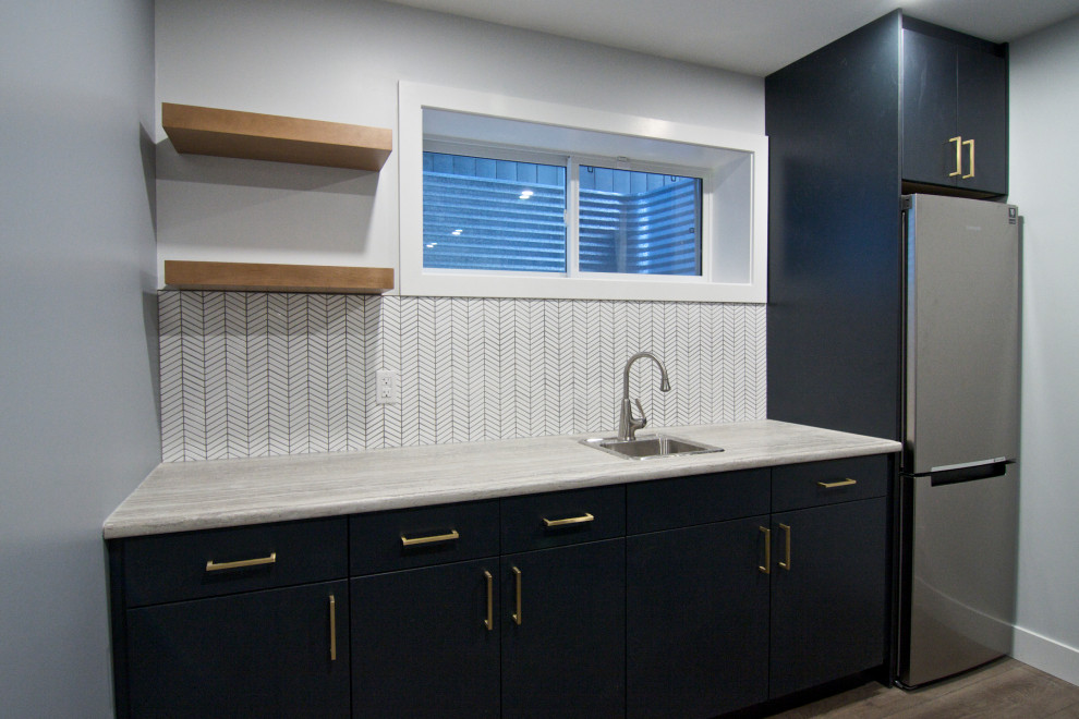 This is an example of a mid-sized modern single-wall wet bar in Edmonton with a drop-in sink, flat-panel cabinets, blue cabinets, laminate benchtops, white splashback, ceramic splashback, vinyl floors, brown floor and white benchtop.