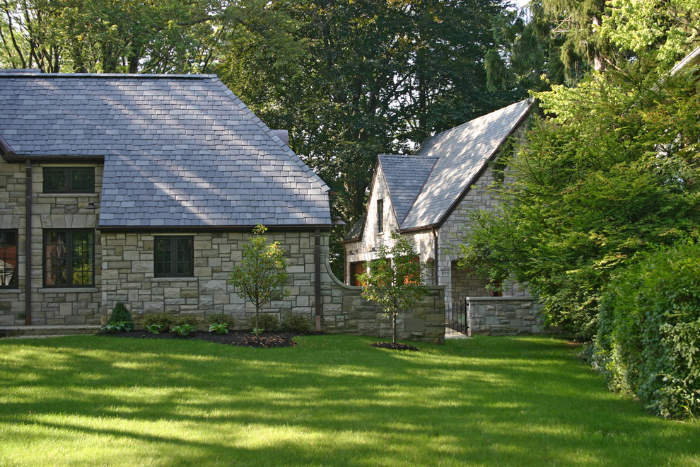 Mid-sized traditional two-storey house exterior in Other with a gable roof, stone veneer and a tile roof.
