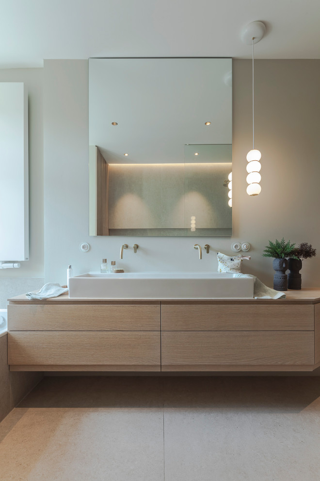 Large modern master bathroom in Munich with flat-panel cabinets, light wood cabinets, a drop-in tub, a curbless shower, a two-piece toilet, beige tile, ceramic tile, grey walls, pebble tile floors, a vessel sink, wood benchtops, beige floor, an open shower, a double vanity, a floating vanity and wood walls.