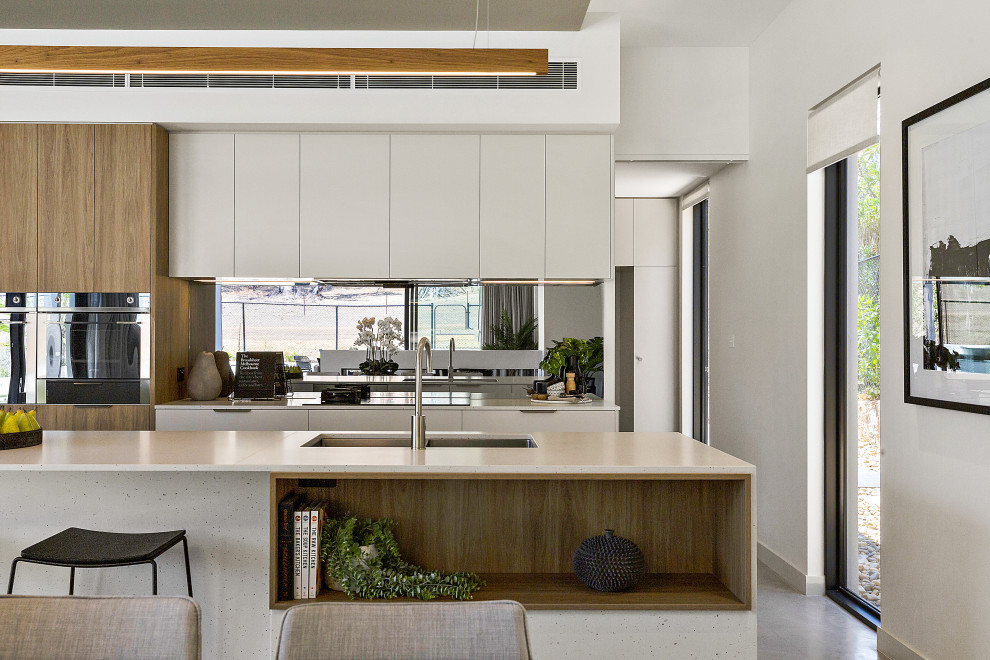 This is an example of a mid-sized contemporary single-wall eat-in kitchen in Canberra - Queanbeyan with an undermount sink, flat-panel cabinets, white cabinets, quartz benchtops, metallic splashback, mirror splashback, black appliances, concrete floors, with island, grey floor and white benchtop.