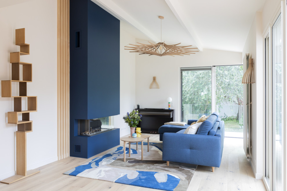 На фото: большая открытая гостиная комната в скандинавском стиле с синими стенами, светлым паркетным полом, стандартным камином, фасадом камина из бетона и многоуровневым потолком с