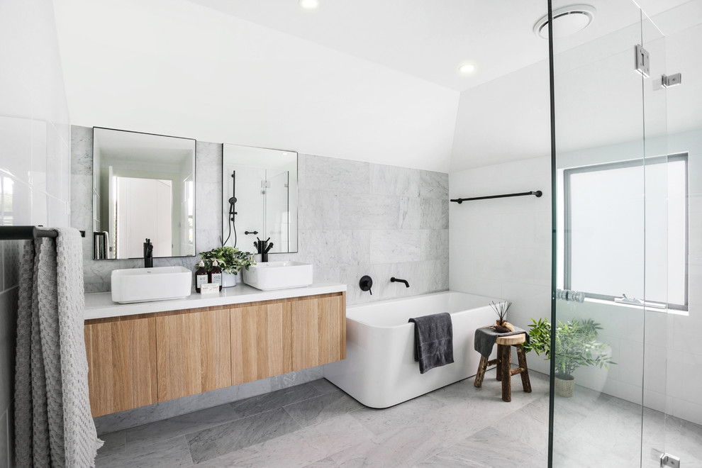 Design ideas for a contemporary bathroom in Sydney with flat-panel cabinets, light wood cabinets, a freestanding tub, an alcove shower, white tile, gray tile, ceramic tile, white walls, ceramic floors, engineered quartz benchtops, grey floor, a hinged shower door, white benchtops and a vessel sink.
