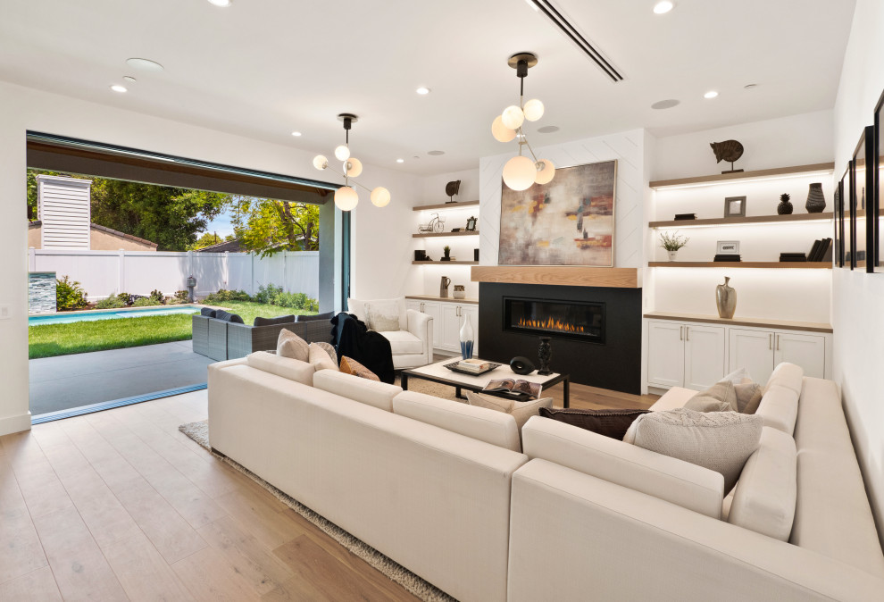 Photo of a large country formal open concept living room in Los Angeles with white walls, light hardwood floors, a standard fireplace, a plaster fireplace surround, no tv and panelled walls.
