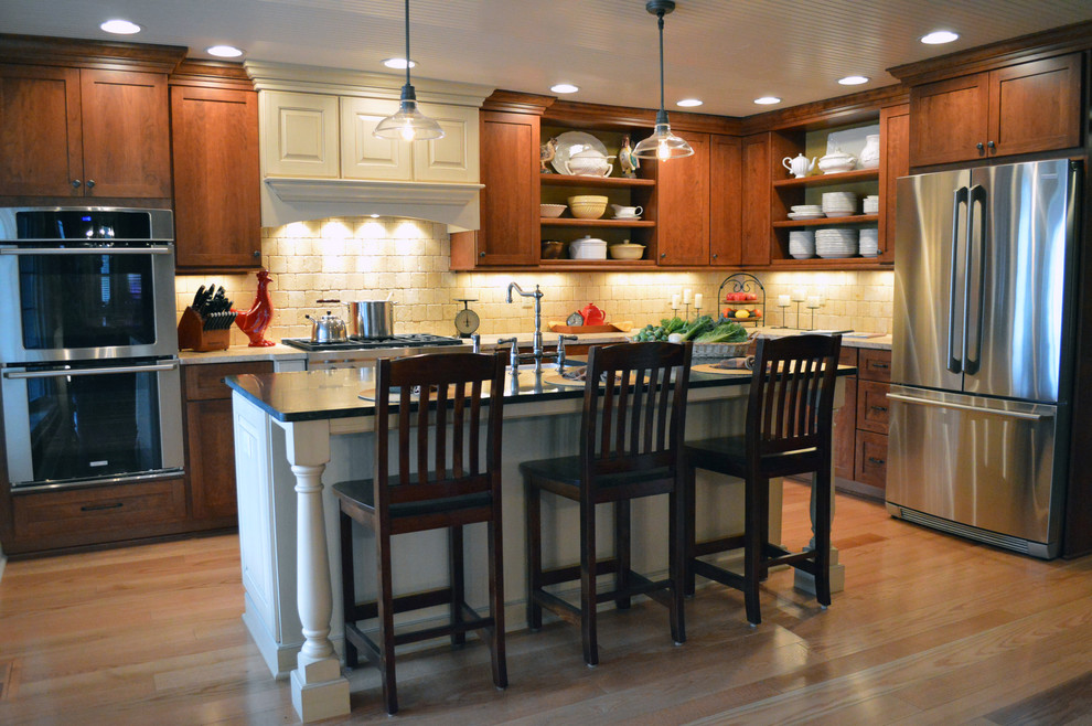Example of a mid-sized classic l-shaped eat-in kitchen design in Columbus with a farmhouse sink, flat-panel cabinets, distressed cabinets, soapstone countertops, beige backsplash, stone tile backsplash, stainless steel appliances and an island