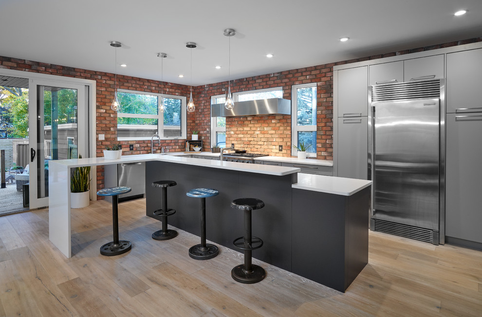 Inspiration for a mid-sized industrial l-shaped kitchen in Edmonton with flat-panel cabinets, grey cabinets, stainless steel appliances, light hardwood floors and with island.