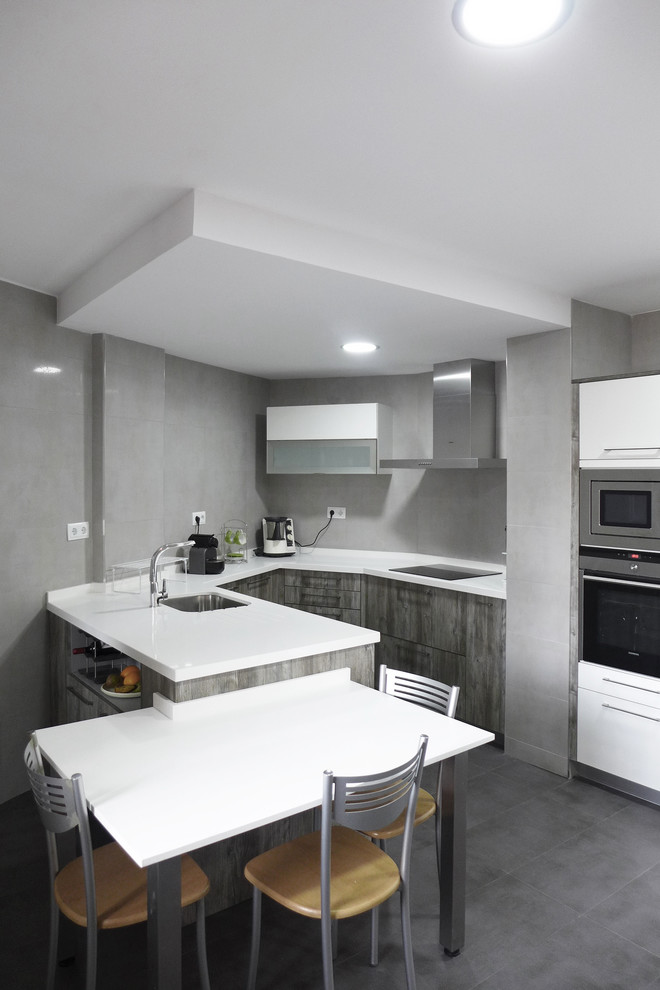 Photo of a large contemporary u-shaped separate kitchen in Madrid with an undermount sink, flat-panel cabinets, white cabinets, quartz benchtops, grey splashback, porcelain splashback, stainless steel appliances, porcelain floors, a peninsula and grey floor.