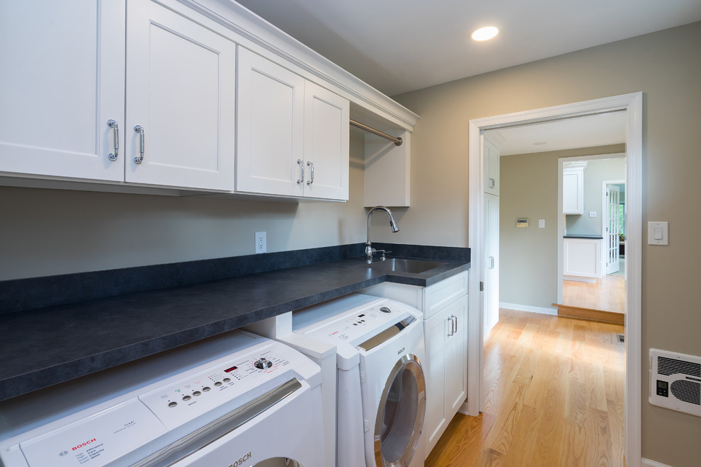 Photo of a mid-sized transitional single-wall dedicated laundry room in Philadelphia with an undermount sink, flat-panel cabinets, white cabinets, quartz benchtops, beige walls, medium hardwood floors, a side-by-side washer and dryer, brown floor and grey benchtop.