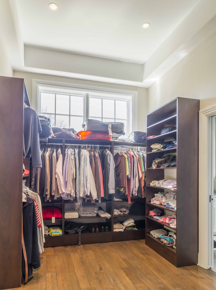 Photo of a mid-sized transitional gender-neutral walk-in wardrobe in Chicago with medium hardwood floors, brown floor, open cabinets, dark wood cabinets and recessed.